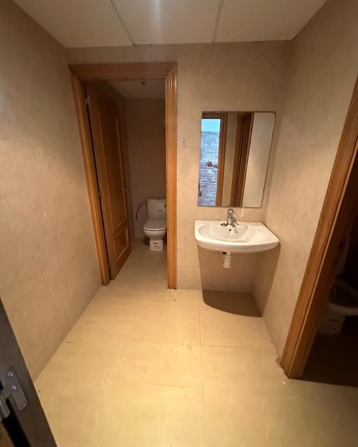 Aseo antiguo con carpintería de madera barnizada, lavabo de pie y paredes en tono crema.