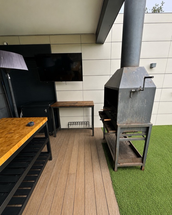 Terraza con la antigua barbacoa metálica exenta y una mesa auxiliar de madera.