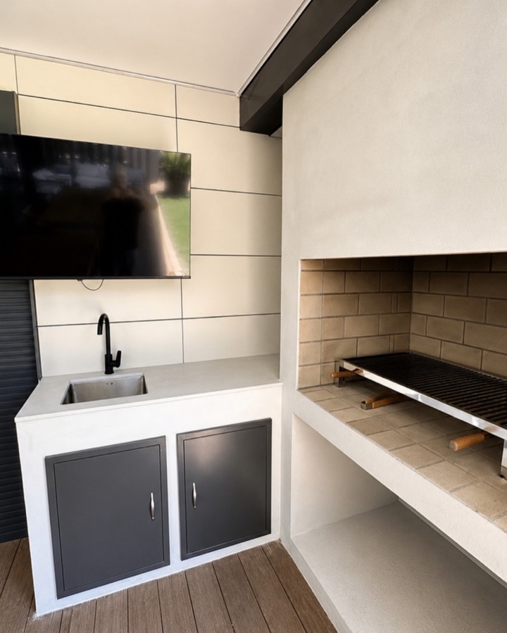 Cocina exterior de obra con encimera, fregadero, armarios y barbacoa empotrada.