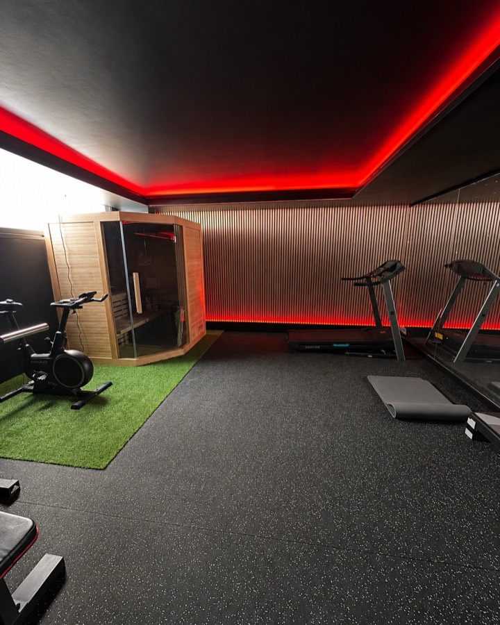 Gimnasio terminado con pavimento de caucho, panelado acústico, luz LED roja y sauna.