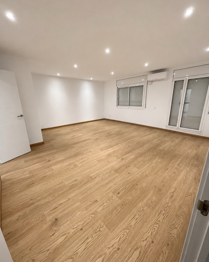 Salón terminado con suelo de madera, paredes blancas y focos LED empotrados.